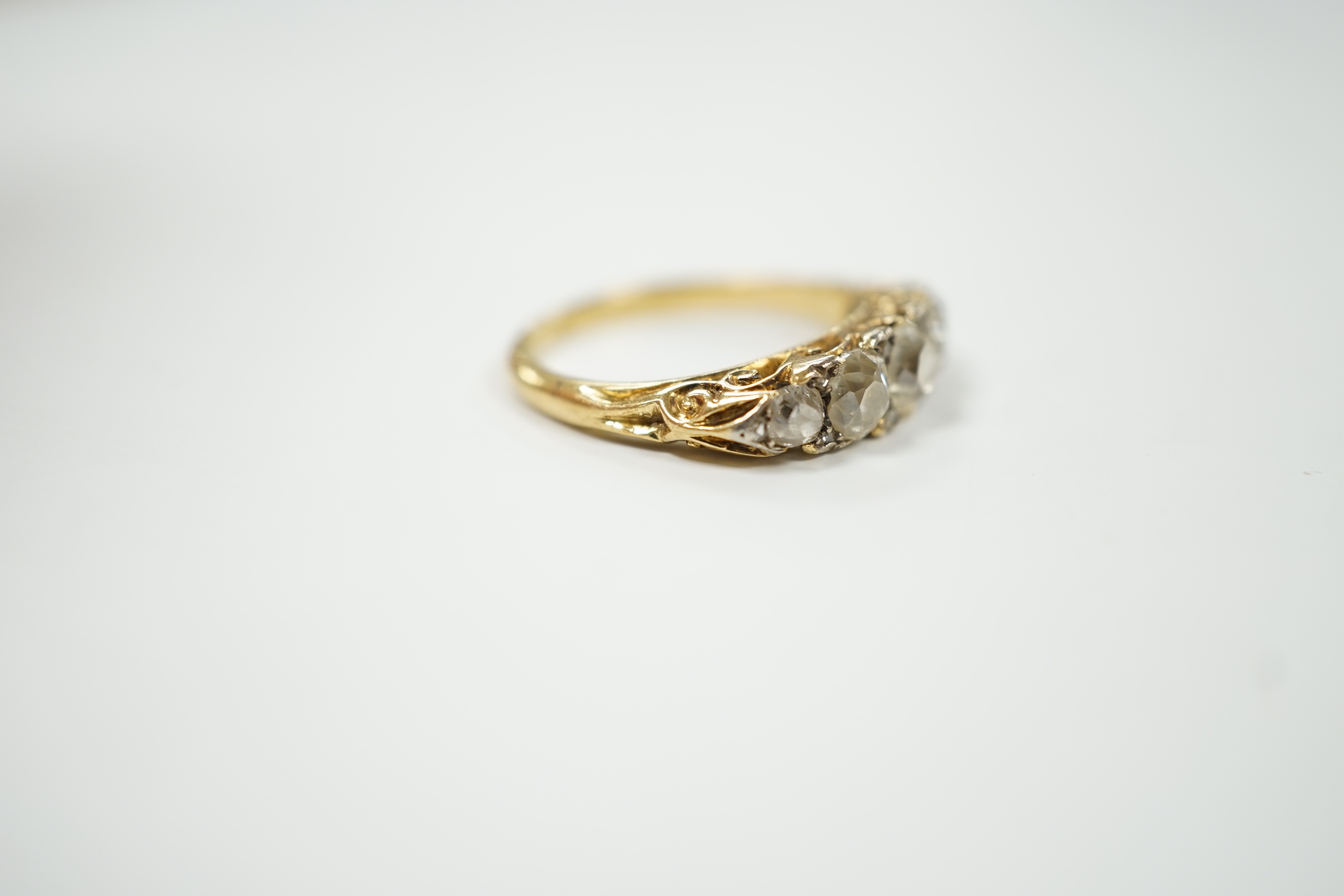 An early 20th century yellow metal and graduated five stone diamond set half hoop ring, with diamond chip spacers, size N/O, gross weight 4.7 grams.